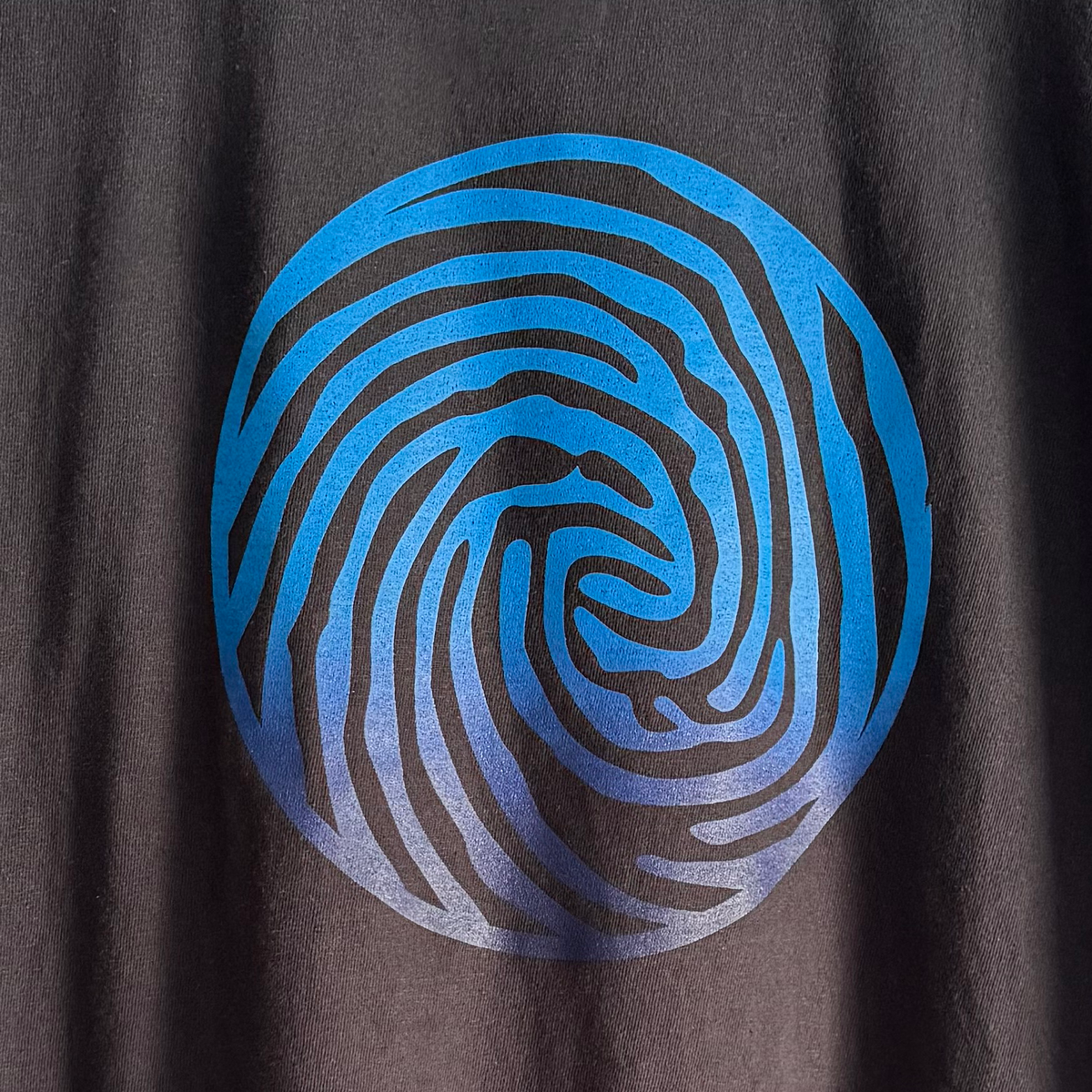 A close-up of a black t-shirt featuring a large circular graphic print with a blue and purple gradient spiral pattern resembling a fingerprint or swirl.