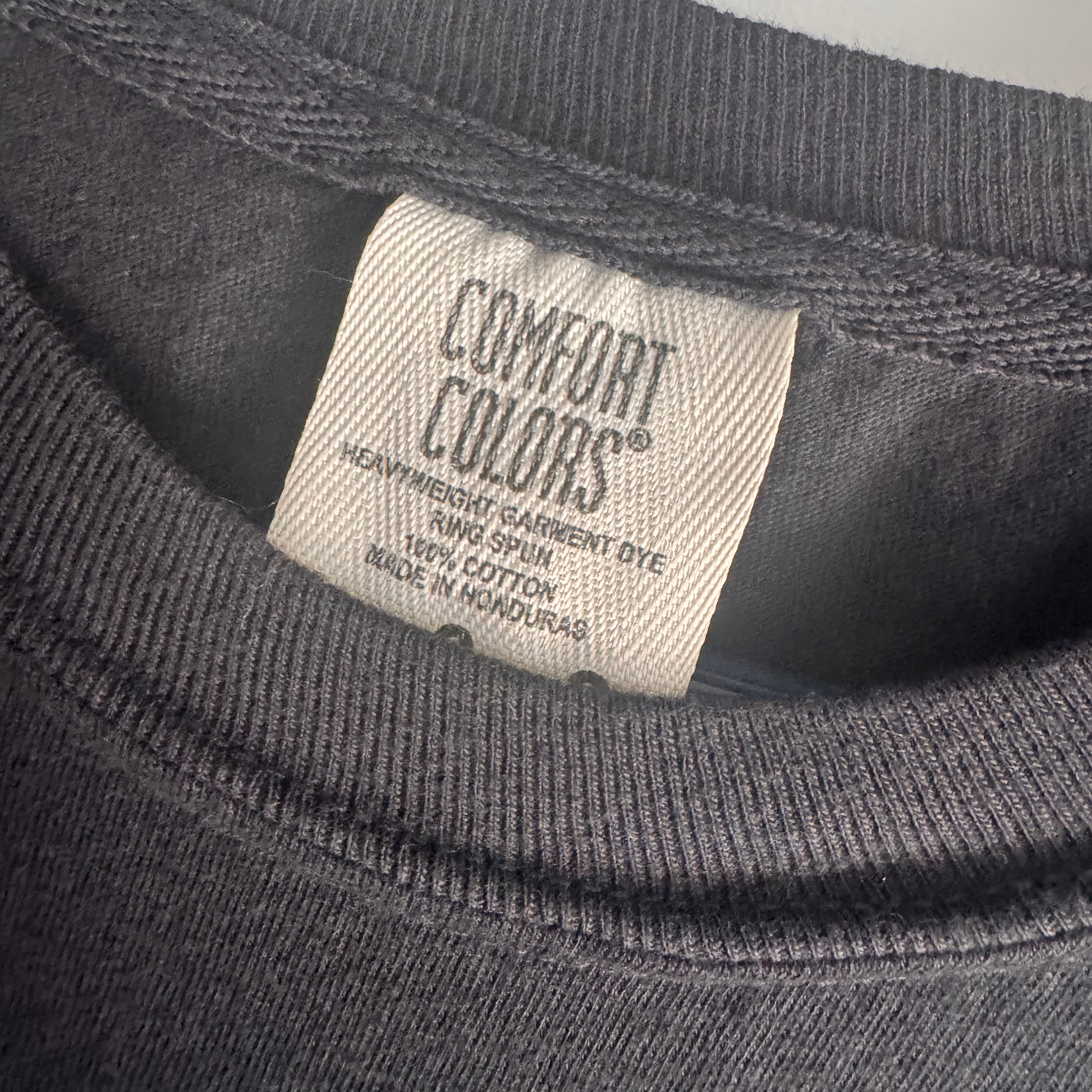 Close-up of the neck label of a dark charcoal gray Comfort Colors t-shirt, showing the brand name and fabric details.