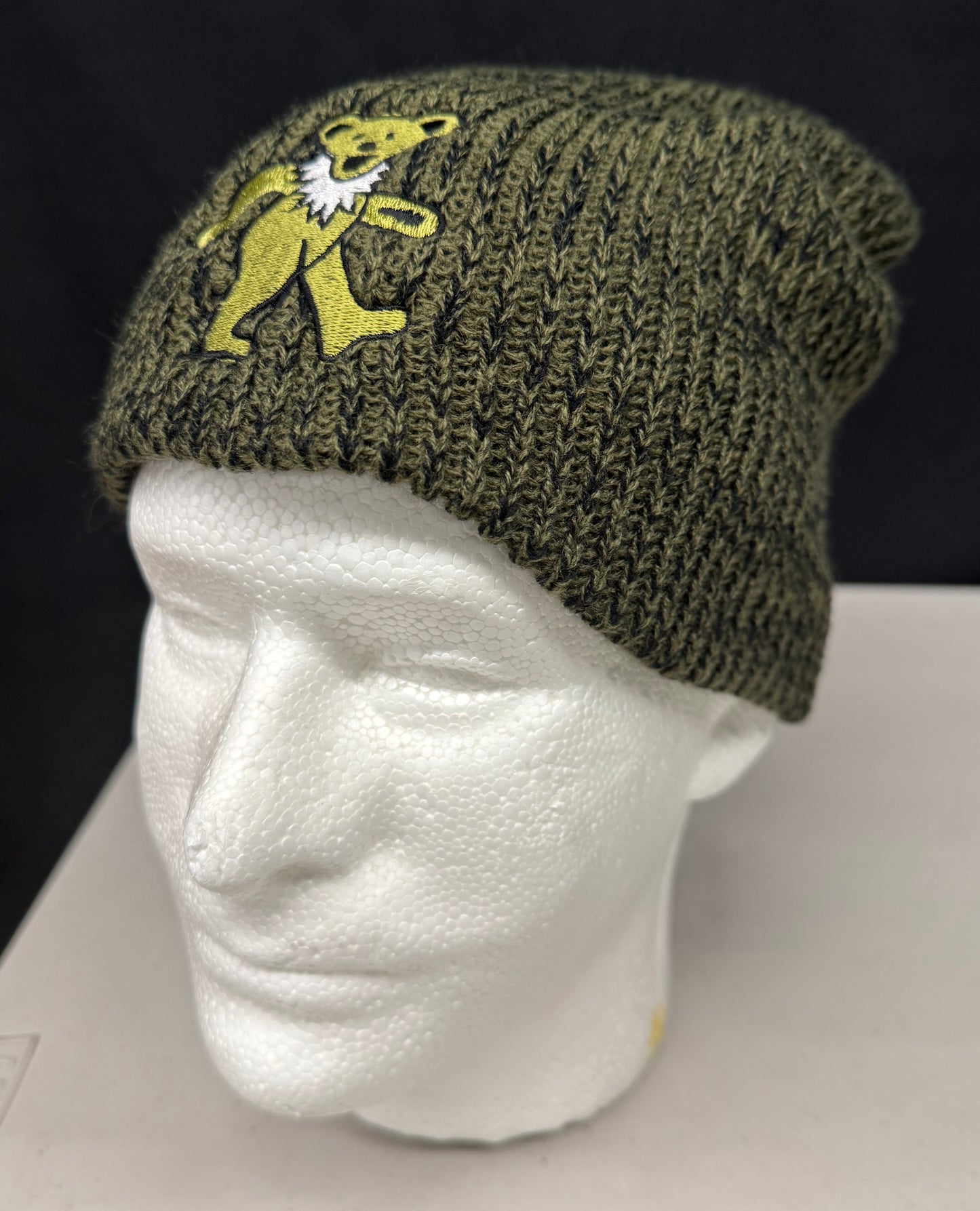 Green knit beanie with a bear logo on a mannequin head against a black background