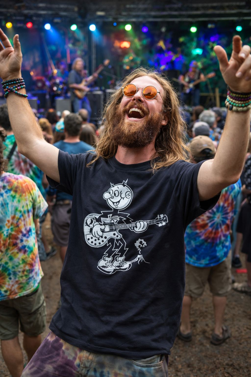 Man with long hair and beard wearing sunglasses and a black t-shirt with a graphic design, standing in a crowd at a concert.