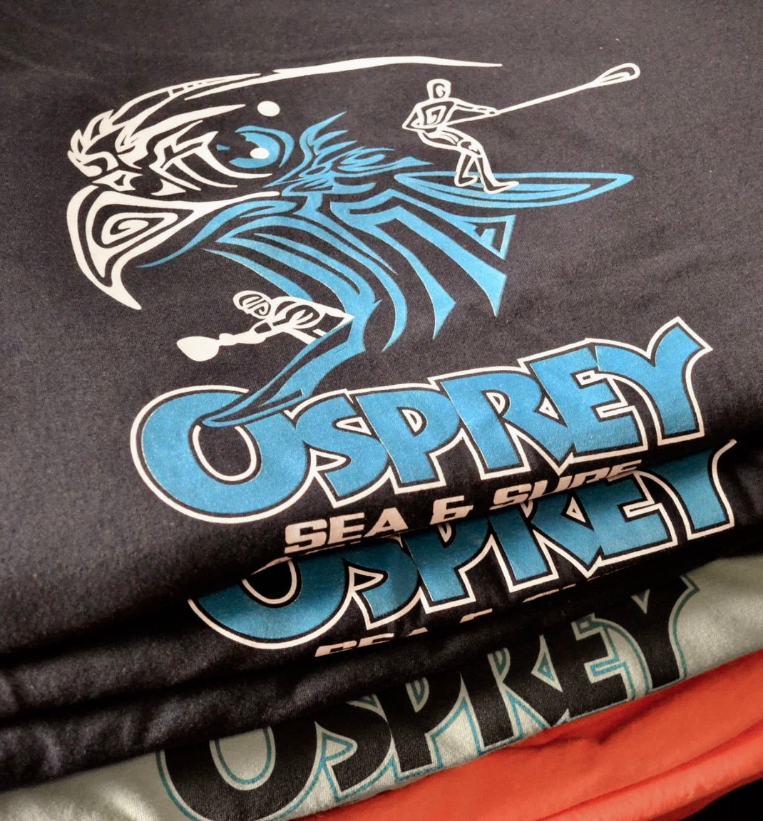Stack of freshly screen printed custom t-shirts with osprey graphic design in a professional print shop setting.